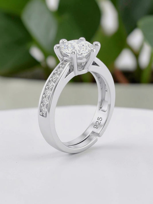 Silver ring with a diamond on a white surface with green leaves in the background